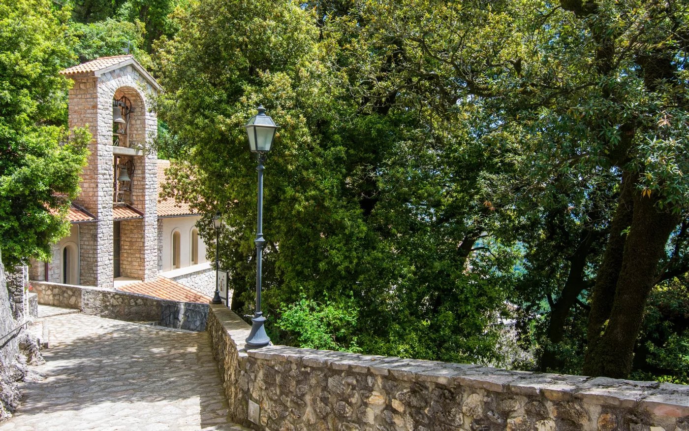 La chiesetta con il campanile a vela e il vialetto acciottolato che sale tra gli alberi sopra Greccio